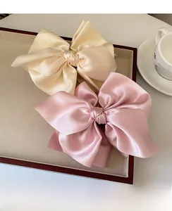 Makro-Detail von übergroßen Satin-Haarschleifen in Beige und Rosa auf einem Holztablett