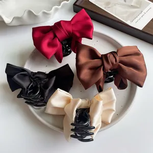 Set of four satin bow hair claws in burgundy, coffee, black, and beige on a plate