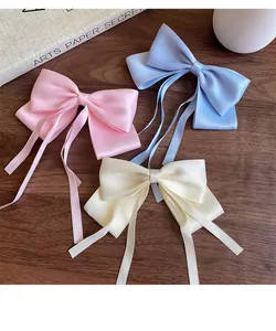 Close-up of three satin bow hair clips in pink, blue, and cream on a wooden desk