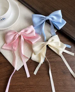 Detailed texture of satin bow hair clips in pink, blue, and cream colors on a desktop