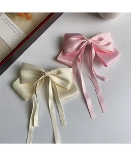 Close-up of pink and cream satin bow hair clips with long elegant ribbons on white desk