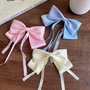 Three elegant satin bow hair clips in pink blue and beige with long streamers on wood