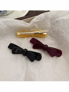 Détail de barrettes nœuds en acétate jaune, rouge et noir sur un plateau en bois
