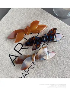 Three acetate bow hair clips in amber, tortoiseshell, and marble patterns on linen