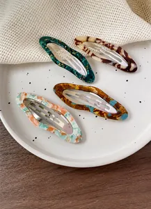 Detailed view of four acetate cloud-shaped hair clips with marble patterns on ceramic plate