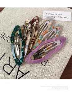 Detail shot of six marble acetate hair clips in various colors on textured fabric