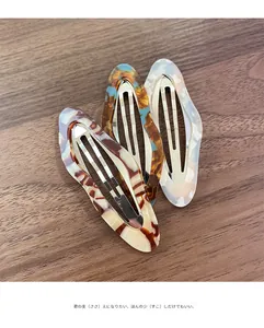 Three acetate marble pattern hair clips displayed on a dark wood background texture