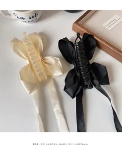 Barrettes à cheveux élégantes avec long ruban en soie noir et crème sur plateau en bois