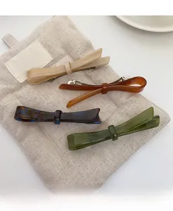 Detail of four acetate bow hair clips in beige and tortoiseshell on linen fabric
