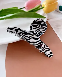 Close-up of zebra pattern hair claw clip with golden logo in an elegant floral setting