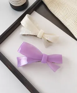 Detail of elegant two-tone bow hair claws in cream and lilac on a decorative background