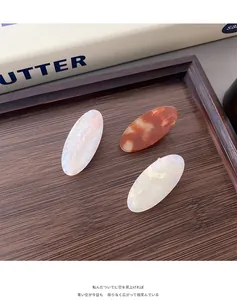 Close-up of three acetate hair claws in tortoise, marble, and pearl on wood tray