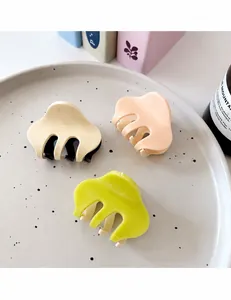 Close-up of minimalist glossy hair claws in cream, pink, and yellow on a display plate