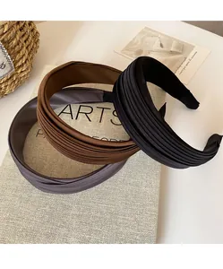 Details von drei plissierten Satin-Haarbändern in Schwarz, Braun und Grau auf einem Buch