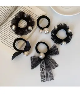 Detail view of five black elastic hair scrunchies with pearls and lace on a white background