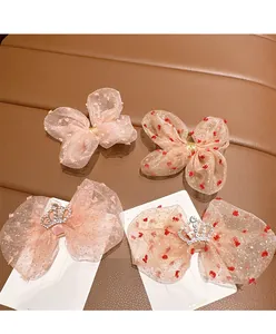 Detail of pink mesh bow hair clips set with sparkling crowns and red pom-poms for girls