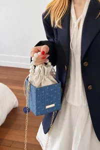 Blue denim crossbody bag with pearl handle and golden chain strap on a model