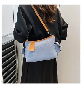 Modell mit hellblauer Jeans-Schultertasche mit braunem Lederbesatz und Seitentaschen