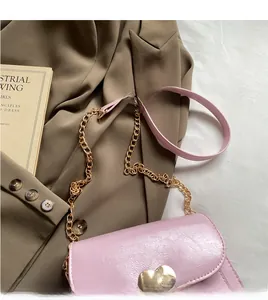 Close-up of light pink crossbody bag featuring a golden heart-shaped buckle and chain strap