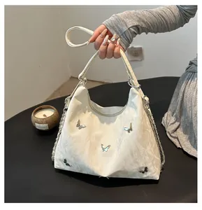 Close-up of white crescent hobo bag with silver butterfly charms and metal chain