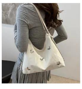 Close-up of white shoulder bag with silver butterfly studs and chain leather strap