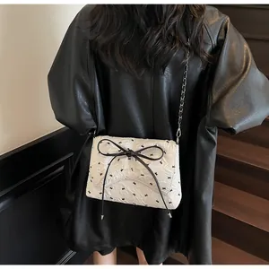 Detail of white pleated crossbody bag with bird embroidery and black leather bow on model