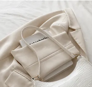 Detalle de bolso baguette blanco textura cocodrilo sobre blazer beige y sábana blanca