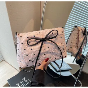 Detail of pink pleated crossbody bag with black bows and metallic chain strap