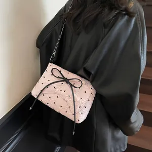 Pink crossbody bag with black rabbit print, oversized bow and chain strap on wood stairs