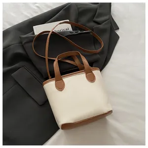 Gros plan du sac seau crème avec poignées marron et détails de couture sur un costume