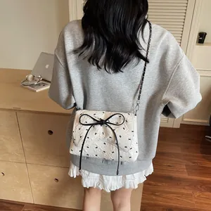 Quilted white crossbody bag with black bow and butterfly embroidery on a desk
