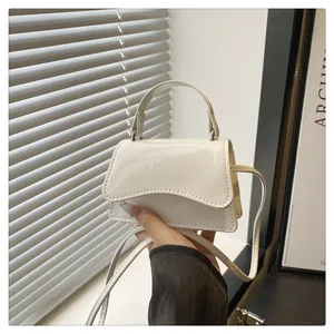Detail of white patent leather mini bag featuring curved flap and top handle for versatile use