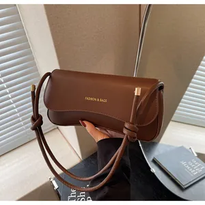 Detail of dark brown leather shoulder bag with gold logo and cylindrical metal hardware