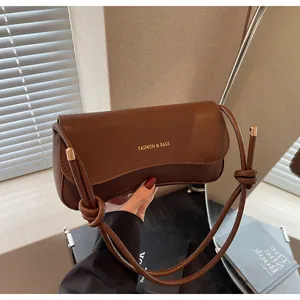 Detail of caramel brown leather bag featuring knotted shoulder strap and gold lettering