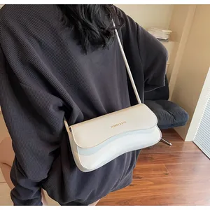 Detail of white PU shoulder bag featuring wave-edged flap and gold logo on leather
