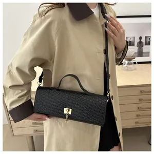Detalle de bolso negro trenzado con broche dorado en modelo con gabardina clásica