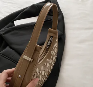 Dettaglio della tracolla regolabile con fibbia argentata su una borsa color kaki con borchie