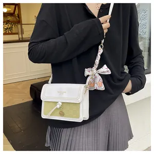 Détail d'un sac bandoulière blanc et vert à motif damier avec foulard en soie décoratif