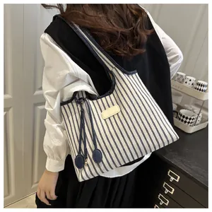 Detalle de bolso tote de lona a rayas azules con borlas decorativas y vista de la bandolera