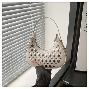 Close-up of cream crescent bag featuring silver metallic studs and smooth PU texture