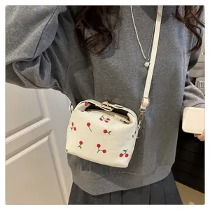 Detailed view of women's cream shoulder bag with red cherry prints and gold metal buckle