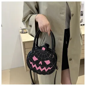 Detail view of a black round pumpkin bag with pink face and adjustable strap on a model