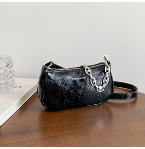 Detail of glossy pleated leather texture and thick silver metal chain on black underarm bag