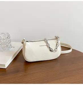 Detail of cream white pleated underarm bag with silver chain and brand lettering on desk