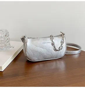 Detail of silver metallic textured crossbody bag with elegant chain and brand logo