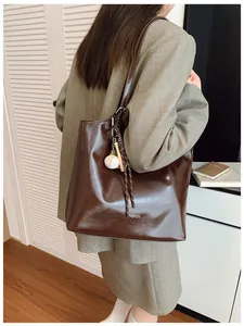 Détail du sac cabas marron en similicuir brillant avec charm de baseball sur la sangle