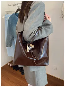 Détail d'un sac cabas marron foncé brillant avec logo et breloques de baseball
