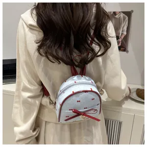 Rear view of a light blue mini backpack with red polka dots and a bow on model