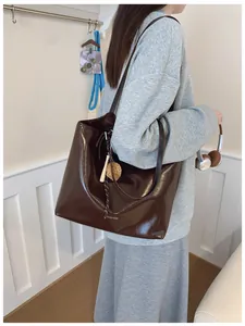 Détail du sac cabas en cuir verni marron foncé avec logo blanc et charms décoratifs