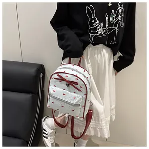 Detailed back view of a white mini backpack with red bow prints on a female model
